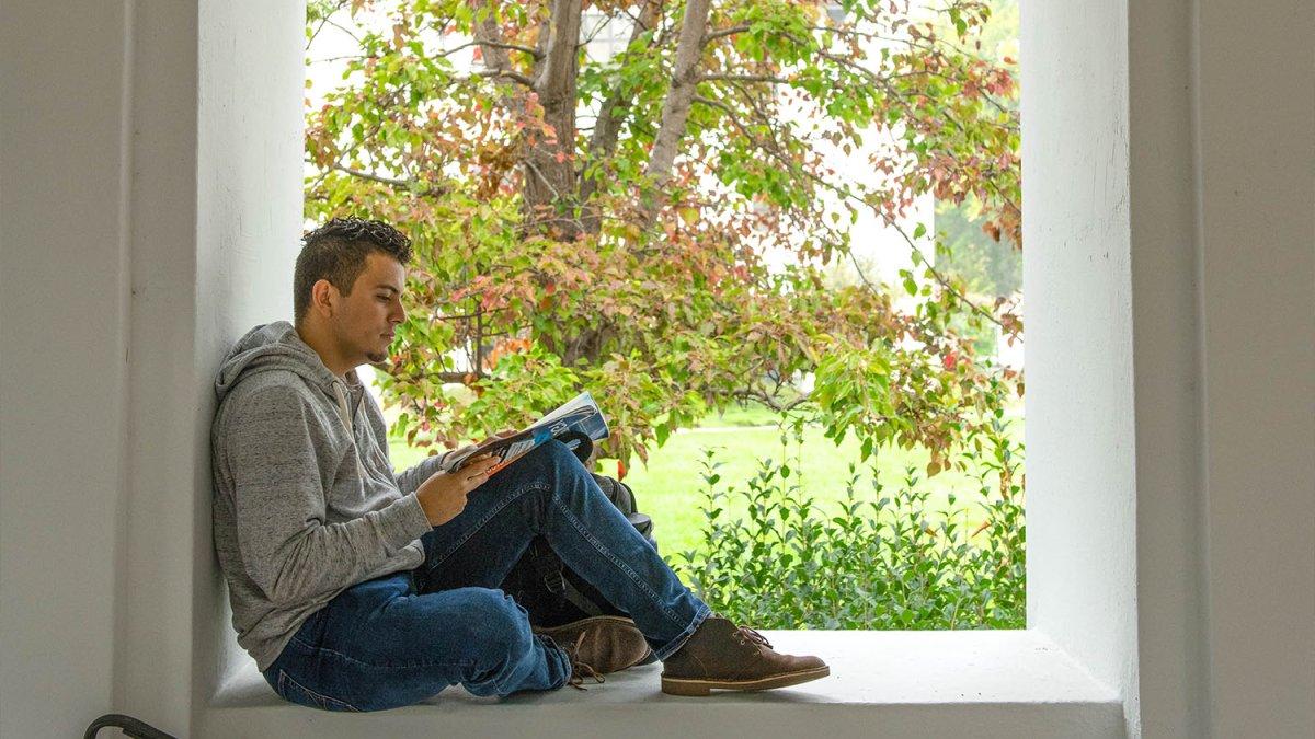 Student reads while sitting on a window seal